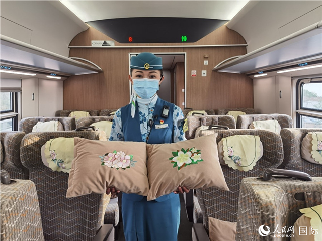 趙瑩靜展示中老鐵路國(guó)際旅客列車?yán)飵в兄袊?guó)牡丹花和老撾占巴花刺繡圖案的靠墊。人民網(wǎng)記者 杜明明攝