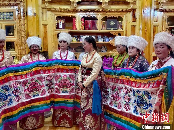 圖為女性展示村民自發(fā)繡制的“百米五彩哈達(dá)”?！±钣穹?攝